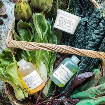 Davines products nestled in a vegetable basket with fresh greens and botanicals