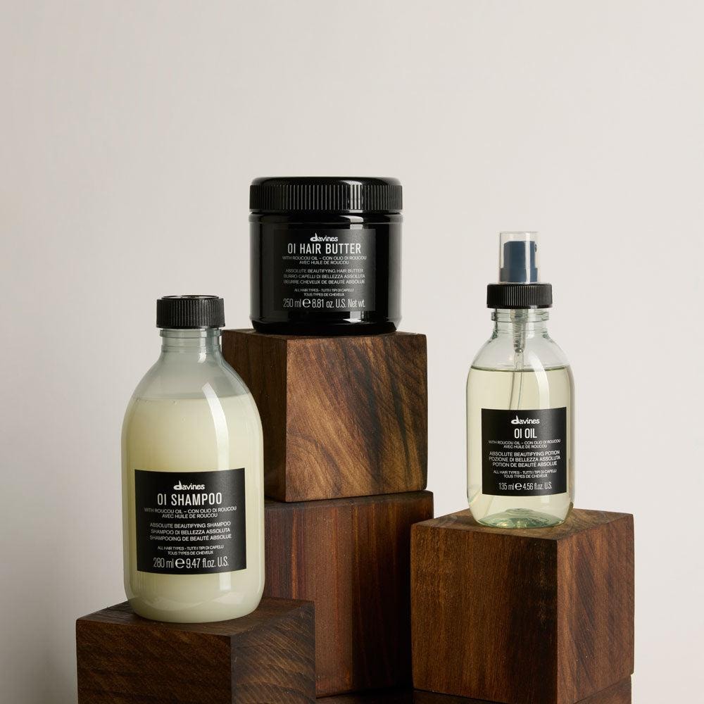 Davines OI Shampoo, OI Hair Butter and OI Oil arranged on wooden blocks against a neutral background